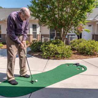 An elderly man enjoys a game of mini-golf on an outdoor putting green in a residential area.