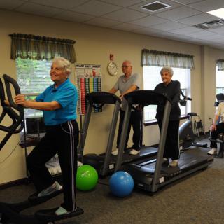 Seniors engaging in fitness activities on treadmills and an elliptical machine in a gym.