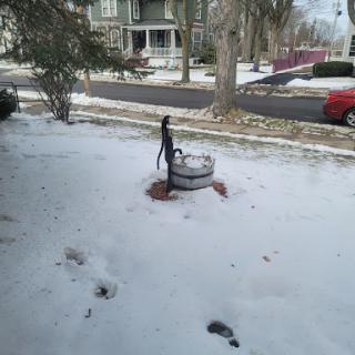 A snow-covered scene featuring an old-fashioned fountain in a residential area.