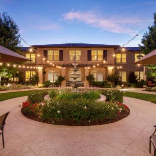 A beautifully landscaped garden with pathways and string lights leads to a two-story house at dusk.