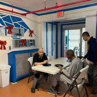 Three people interacting around a dining table in a community setting.