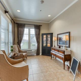 A cozy living room featuring a piano, wicker chairs, and large windows with curtains.