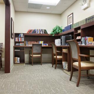 A quiet office space featuring several desks and chairs, surrounded by bookshelves filled with books.