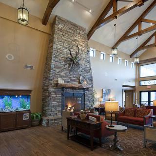 A cozy living room featuring a tall stone fireplace, wood beams on the high ceiling, and comfortable seating.