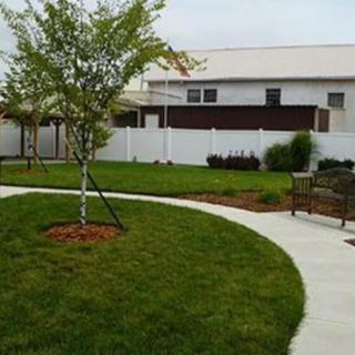 A landscaped garden featuring a tree, grassy area, curving pathway, bench, and a white fence.