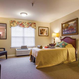A cozy bedroom interior featuring a bed, artwork, and a window providing natural light.