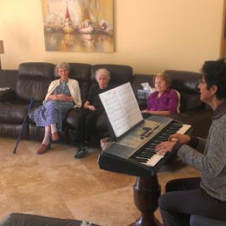 A musician performing for a group of seniors in a cozy living room setting.