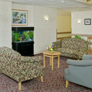 A cozy lobby area featuring two patterned couches, a grey armchair, a central coffee table with flowers, and an aquarium.