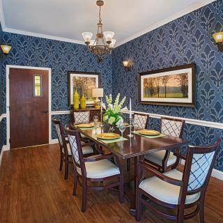 An elegant dining room with ornate wallpaper, a chandelier, and a wooden dining table surrounded by chairs.