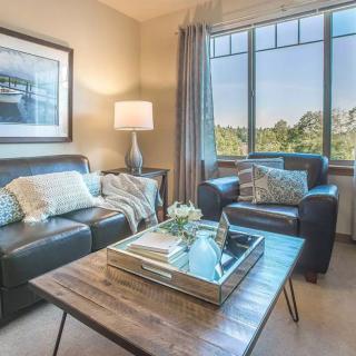 A cozy living room with a leather sofa, armchair, and a wooden coffee table, adorned with decor items and illuminated by a standing lamp beside a large window.