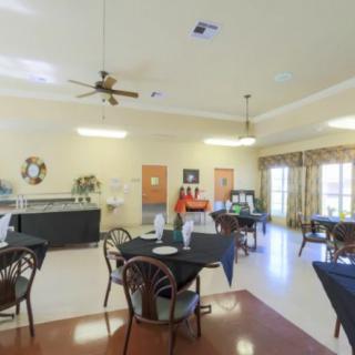 A spacious dining area with multiple tables and chairs, featuring a large window and ceiling fan.