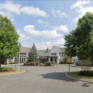 A building entrance surrounded by trees and a clear sky, with a driveway leading up to it.
