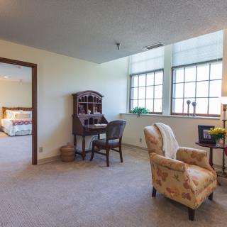 A cozy living room area with a desk, armchair, and large windows.