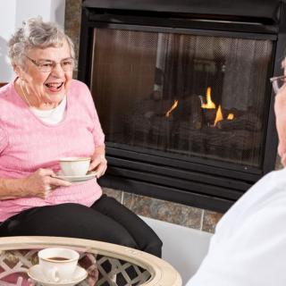 Elderly couple enjoying coffee by the fireplace.