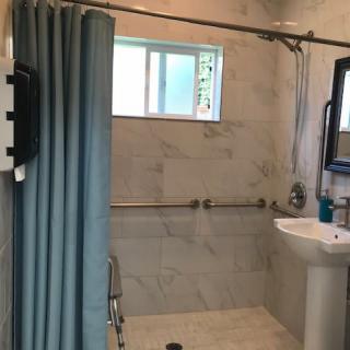 A bathroom with a shower area featuring a curtain, grab bars, and a sink.