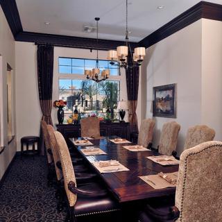 A luxurious dining room with a long wooden table, upholstered chairs, and a chandelier hanging from the ceiling.