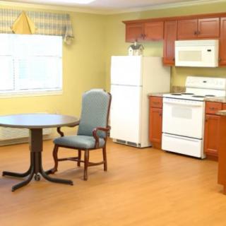 A cozy kitchen with wooden cabinetry, featuring a dining table and chair, along with essential appliances like a refrigerator and stove.