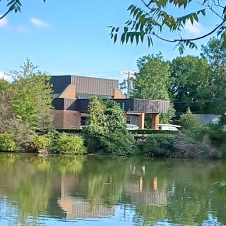 A modern house set against a serene lake, surrounded by lush greenery.