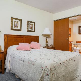 A cozy bedroom featuring a wooden bed with a floral quilt and pink pillows, flanked by nightstands and lamps, with framed artwork on the walls.