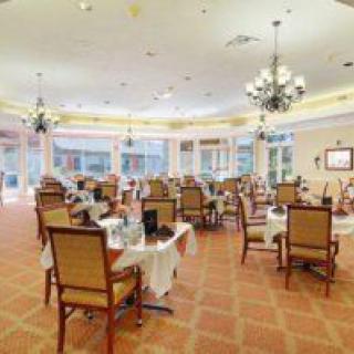 A spacious dining room with elegantly set tables and chairs, featuring chandeliers and large windows.