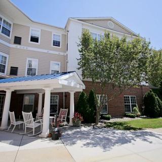 A sunny day with a view of a residential building featuring an outdoor patio area with chairs and greenery.