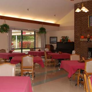 A cozy dining area with tables covered in red tablecloths and arranged neatly, featuring natural light from large windows.