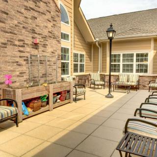 A well-furnished patio area with chairs and a bench, surrounded by a brick wall and large windows.