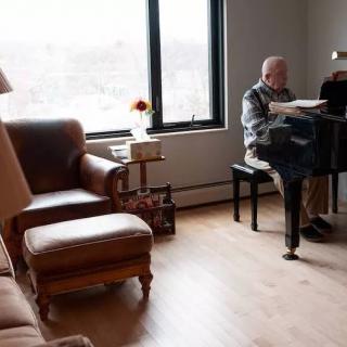 A man playing the piano in a cozy living room with natural light coming through the window.