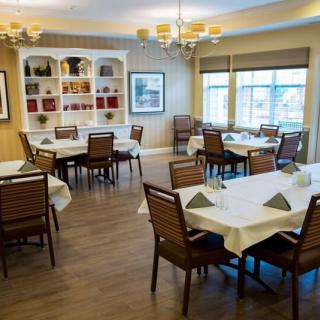 A well-lit dining room with neatly arranged tables and chairs, featuring elegant chandeliers and large windows.