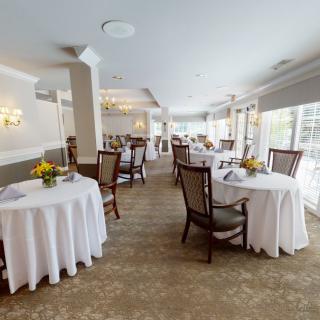 An elegant restaurant dining room with neatly arranged tables covered in white tablecloths.
