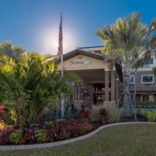 A well-landscaped building entrance with palm trees and a flag under a clear blue sky.