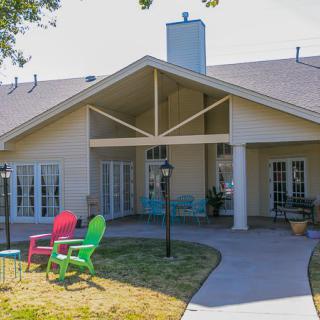A backyard view of a house with a patio and colorful chairs on the lawn.