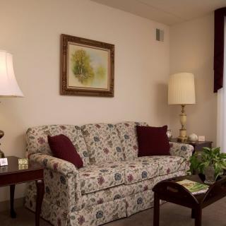 A cozy living room with a floral sofa, two lamps, a painting on the wall, and a small plant.