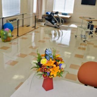 A rehabilitation center room with exercise equipment and a floral arrangement on a table.