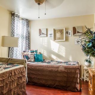 A cozy and well-decorated bedroom featuring two beds, patterned curtains, decorative pillows, framed wall art, and a touch of natural light.