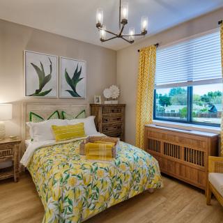 A cozy bedroom with yellow accents and botanical artwork, featuring a neatly made bed and elegant lighting.