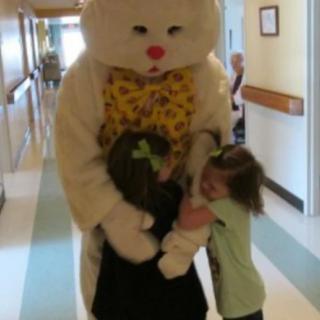 Two children hugging a person in an Easter bunny costume in a hospital hallway.