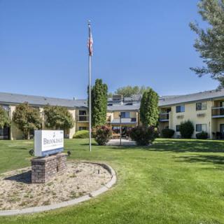 A sunny day view of a building with a neatly landscaped lawn, featuring a flagpole and signage in the foreground.