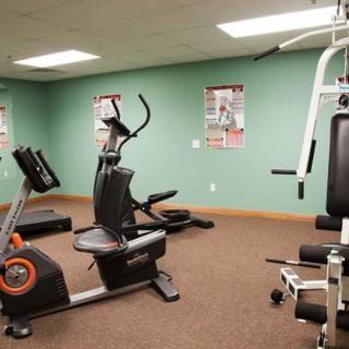 A gym with various exercise equipment including a stationary bike, an elliptical machine, and a weight lifting station.