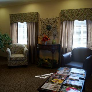 A cozy waiting room with chairs, a coffee table adorned with magazines, and sunlight streaming through the windows.