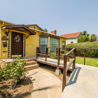 A charming yellow house with a ramp and a well-maintained front yard on a sunny day.