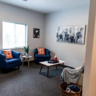 A cozy living room with blue chairs, a window, and wall art.
