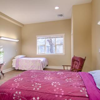 A cozy bedroom with two beds, a window, and a rocking chair.