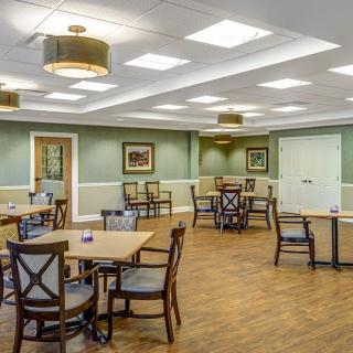 A spacious dining room with neatly arranged tables and chairs, soft lighting, and a wooden floor.