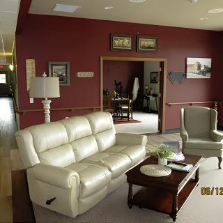 A cozy living room with a white leather sofa, an armchair, and a wooden coffee table against a maroon wall.
