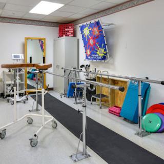 A well-equipped physical therapy room featuring balance bars, exercise mats, and a walking track to aid rehabilitation.