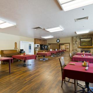 A spacious dining area with wooden floors and tables covered with red tablecloths.