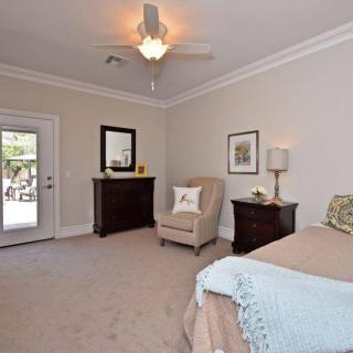 A modern bedroom with neutral decor, featuring a comfortable chair and a bedside lamp.