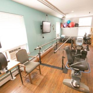 A rehabilitation room equipped with exercise and therapy equipment, including parallel bars and chairs.