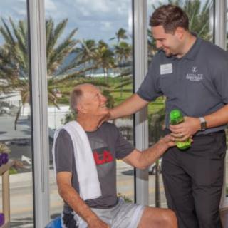 A fitness trainer supporting an elderly man during his workout session at the gym.